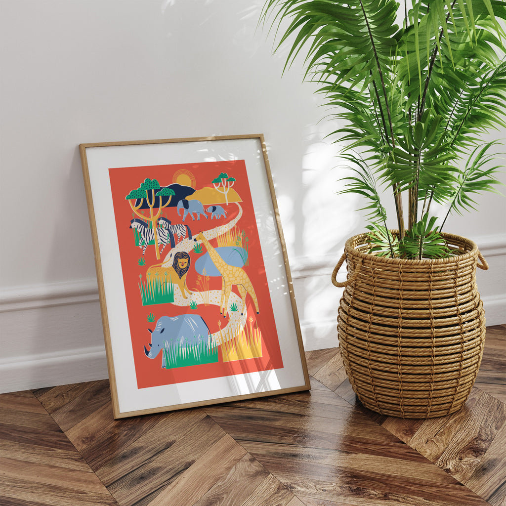 A bold print featuring a safari scene filled with lions, zebras and giraffes on a red background. Art print is framed and leaning against a wall next to a green potted plant.