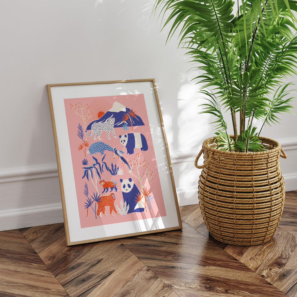A pastel art print featuring an exotic scene filled with pandas, pangolins and lions on a pink background. Art print is framed and leaning against a wall.